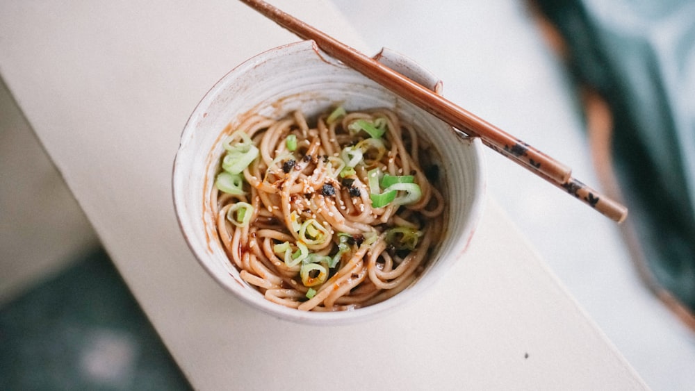 white ceramic bowl with noodles and chopsticks