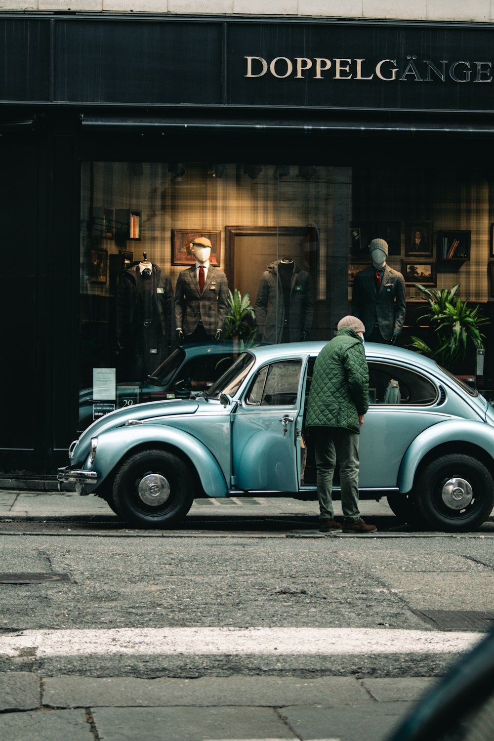 man in green jacket standing beside blue car during daytime