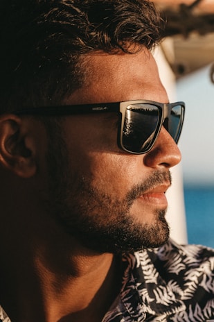 Side profile of a man adjusting his classic aviator sunglasses outdoors on a sunny day.