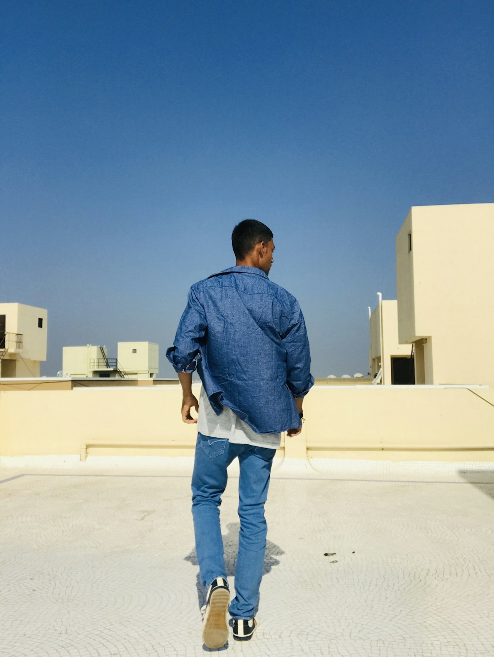 man in blue dress shirt and blue denim jeans standing on white building during daytime
