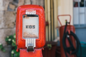 An old red tire inflator machine with a vintage design. The device has a square window displaying the number '05' and various instructions underneath. It is surrounded by a blurred background featuring some additional equipment.