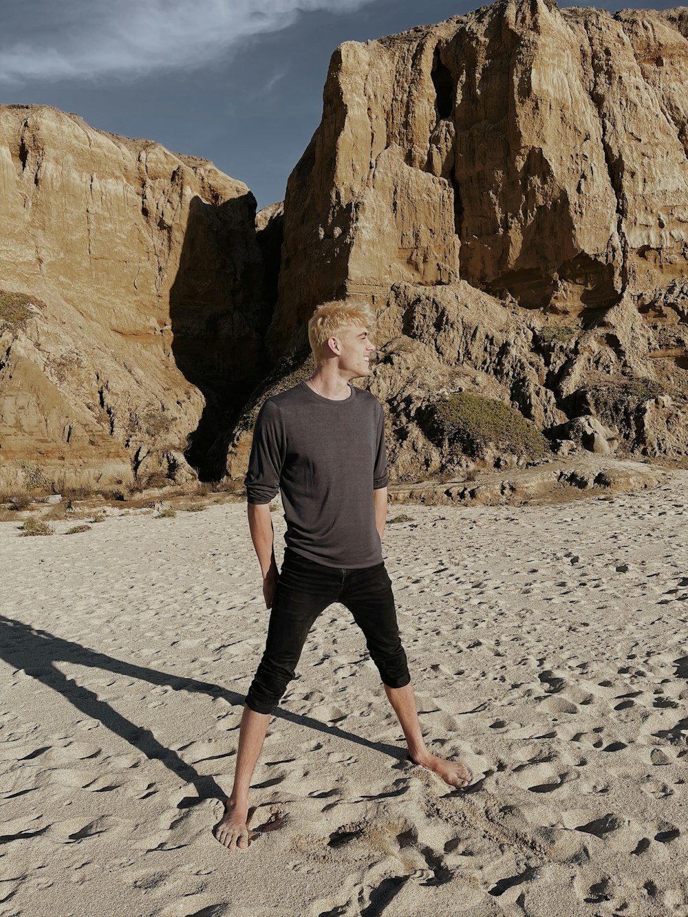 woman in gray long sleeve shirt and black pants standing on gray sand during daytime