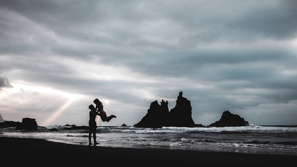 silhouette of 2 people walking on beach shore during sunset