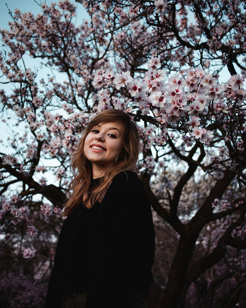 woman in black long sleeve shirt standing under pink cherry blossom tree during daytime