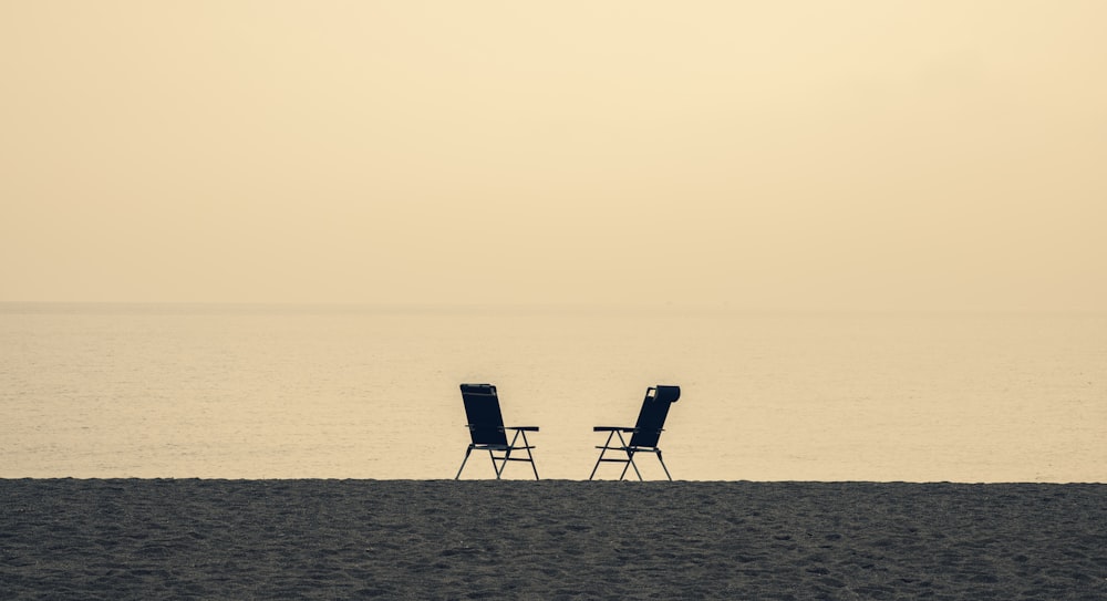 Dos sillas plegables blancas y negras en la playa durante el día