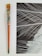 An aged paintbrush with a colorful, paint-splattered handle sits beside an abstract black and white artwork, featuring dynamic white lines crossing over a dark background.