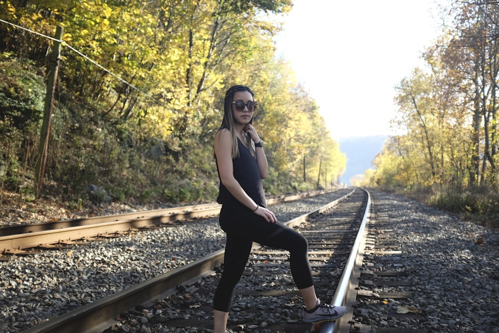 woman in black tank top and black pants standing on train rail during daytime