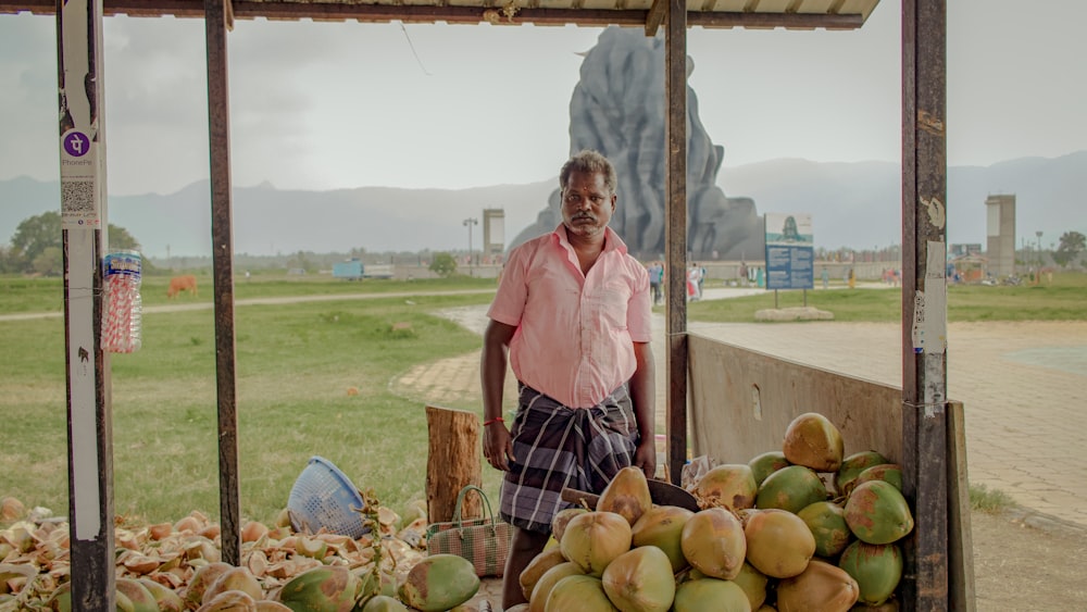 man in pink dress shirt standing near coconut fruits during daytime