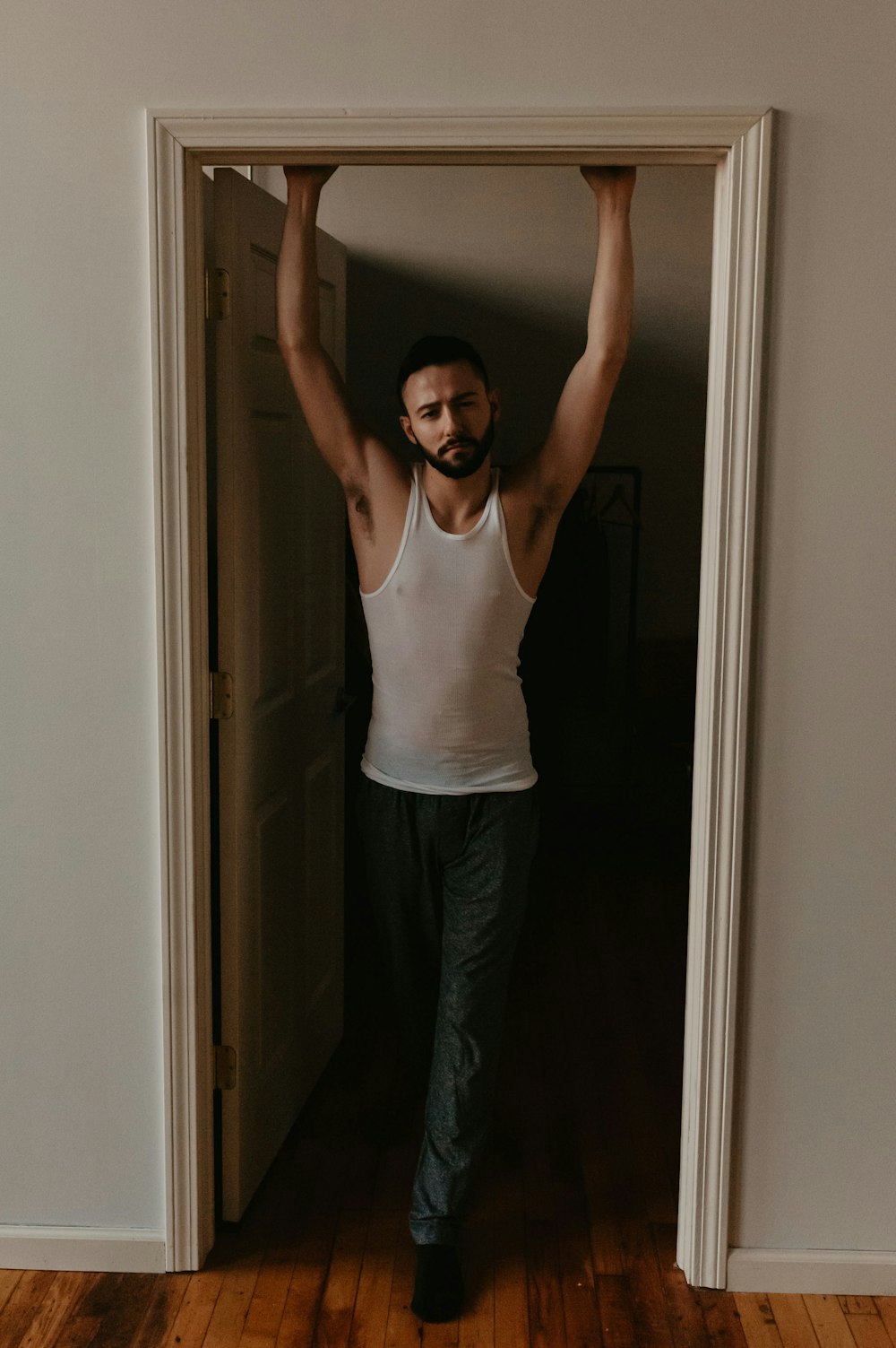 man in white tank top and black pants standing near door