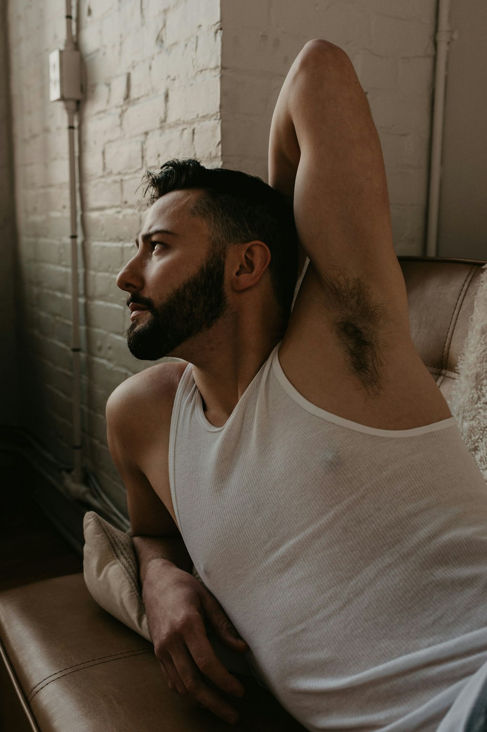 man in white tank top sitting on brown sofa