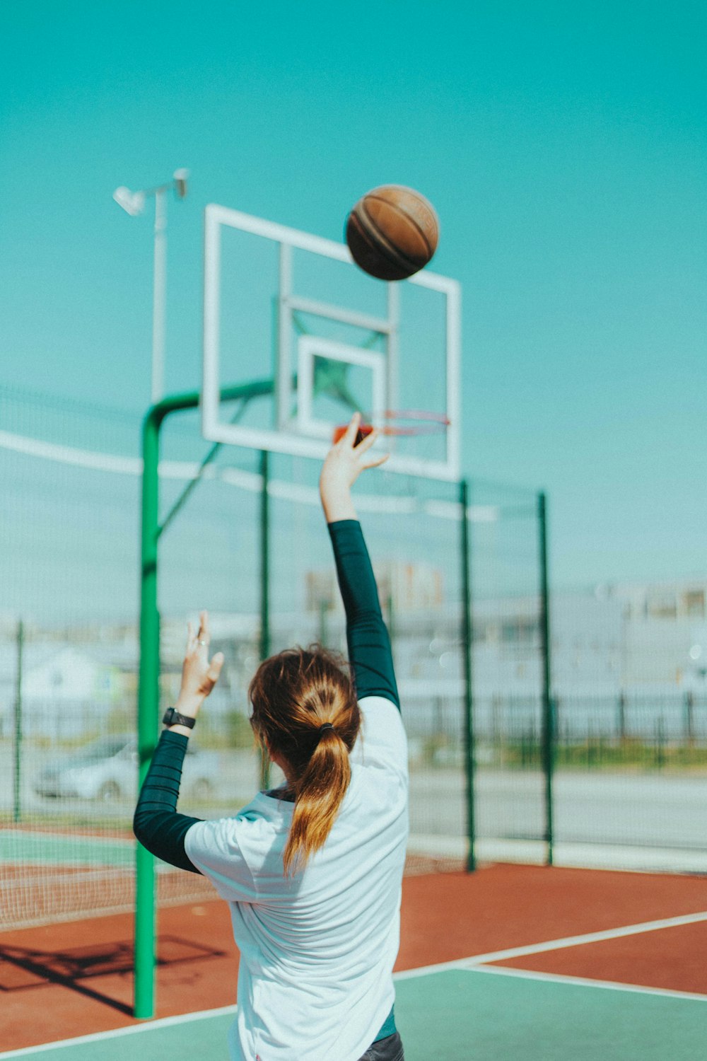 흰색 긴팔 셔츠와 파란색 데님 청바지를 입은 여자가 낮에 농구를 하고 있다