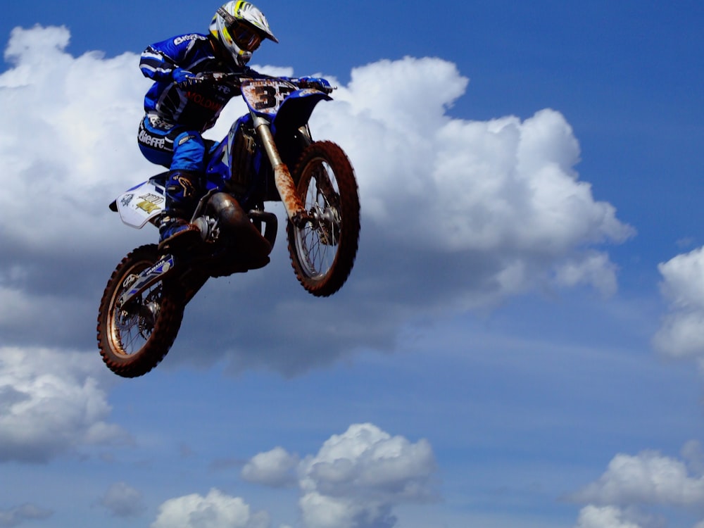 昼間、白い雲と青い空の下で青と黒のスポーツバイクに乗る男