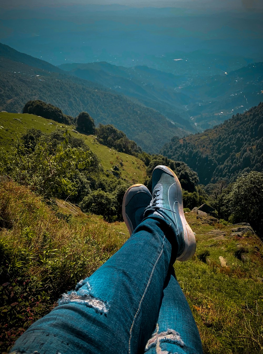 person in blue denim jeans and black and white sneakers sitting on rock mountain during daytime