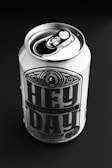 A can of non-alcoholic malt beverage labeled 'Hey Day' with peach flavor, placed on a dark background. The can is metal with a pop-top lid, prominently featuring bold typography and decorative design elements.