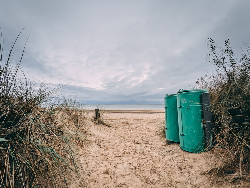 green trash bin on brown sand under white clouds during daytime