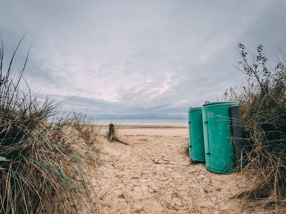 Cubo de basura verde en arena marrón bajo nubes blancas durante el día
