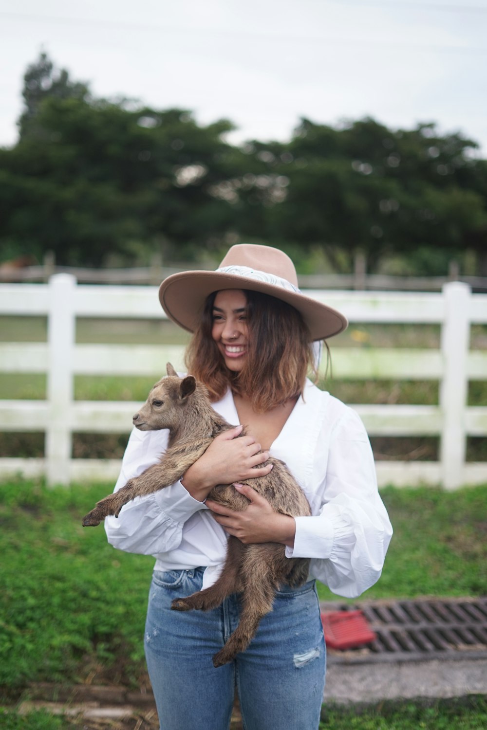 girl in white long sleeve shirt and brown cowboy hat holding brown animal during daytime
