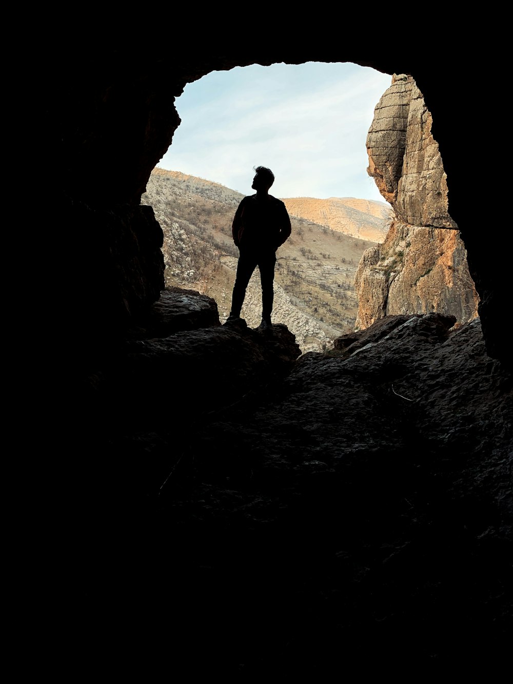 silhouette of man standing on rock formation during daytime