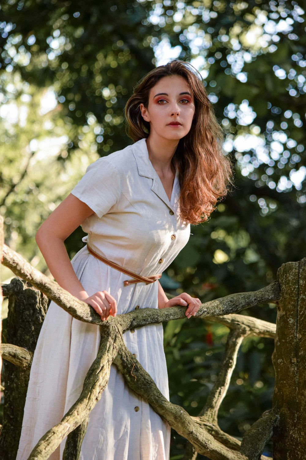 woman in white button up shirt standing beside brown tree during daytime