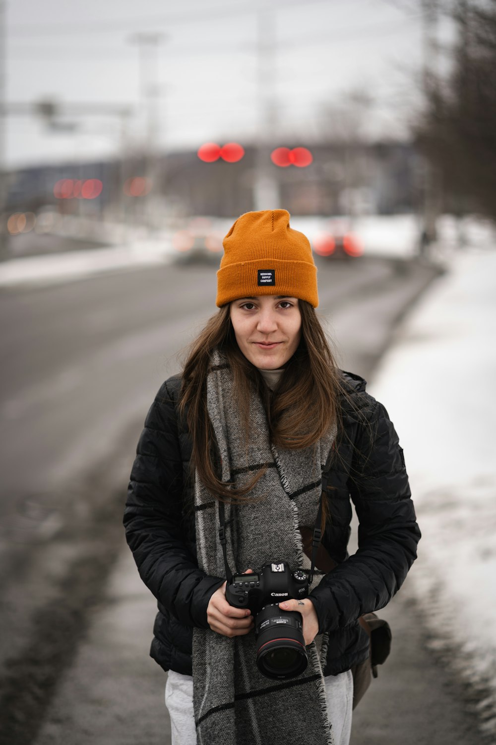 woman in black jacket and orange knit cap holding black dslr camera