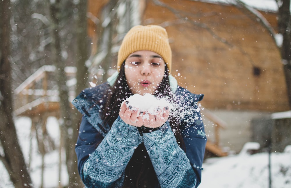 child in blue jacket and yellow knit cap holding snow