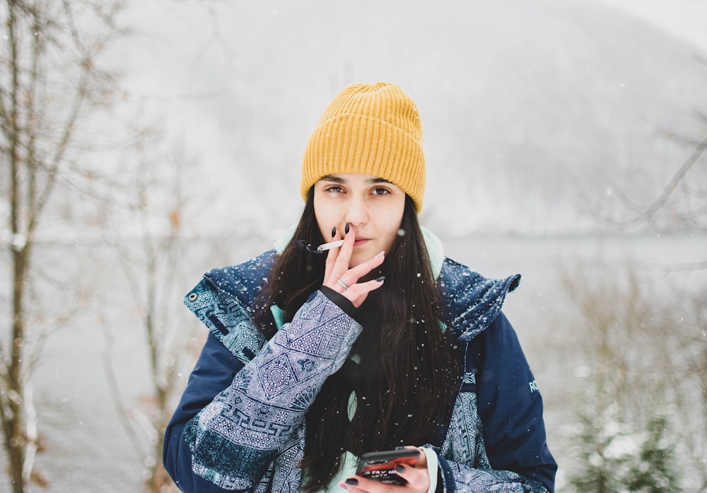 woman in yellow knit cap and black and white coat holding smartphone