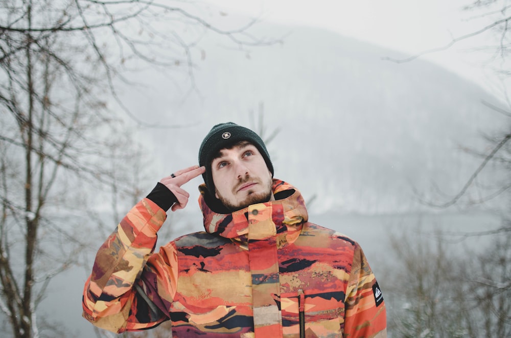 Hombre con sudadera con capucha de camuflaje marrón y negro de pie en suelo cubierto de nieve durante el día