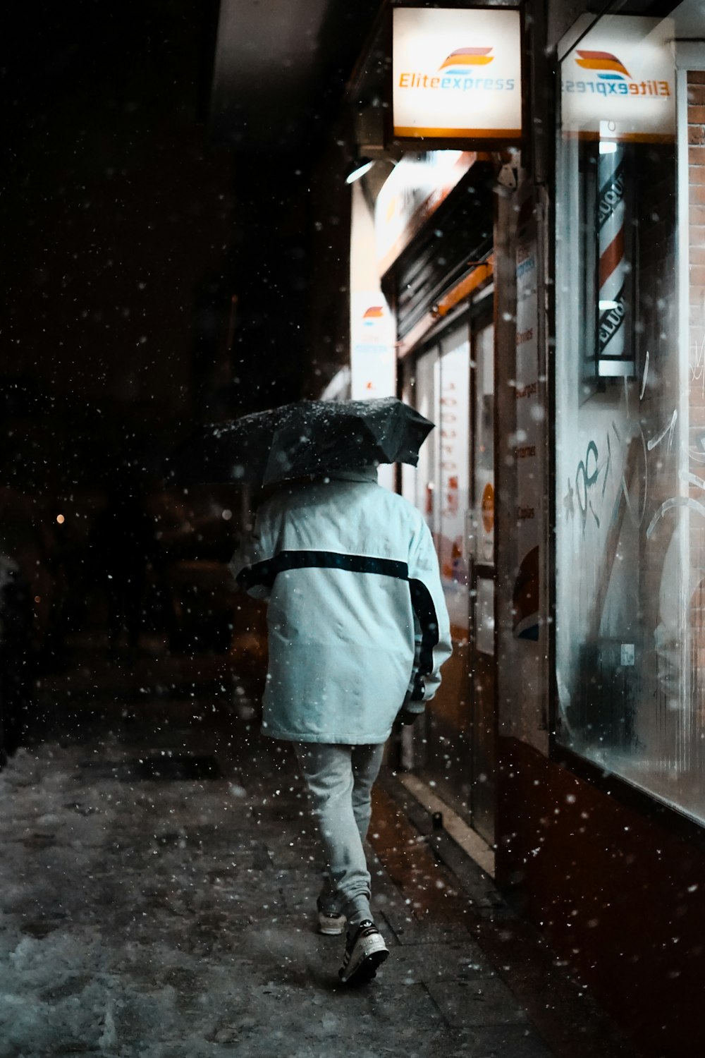 person in white shirt and gray pants with black umbrella standing on sidewalk during night time