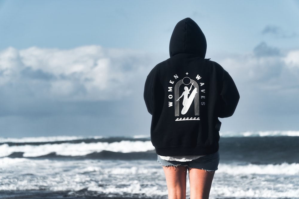 pessoa em hoodie preto em pé na costa durante o dia