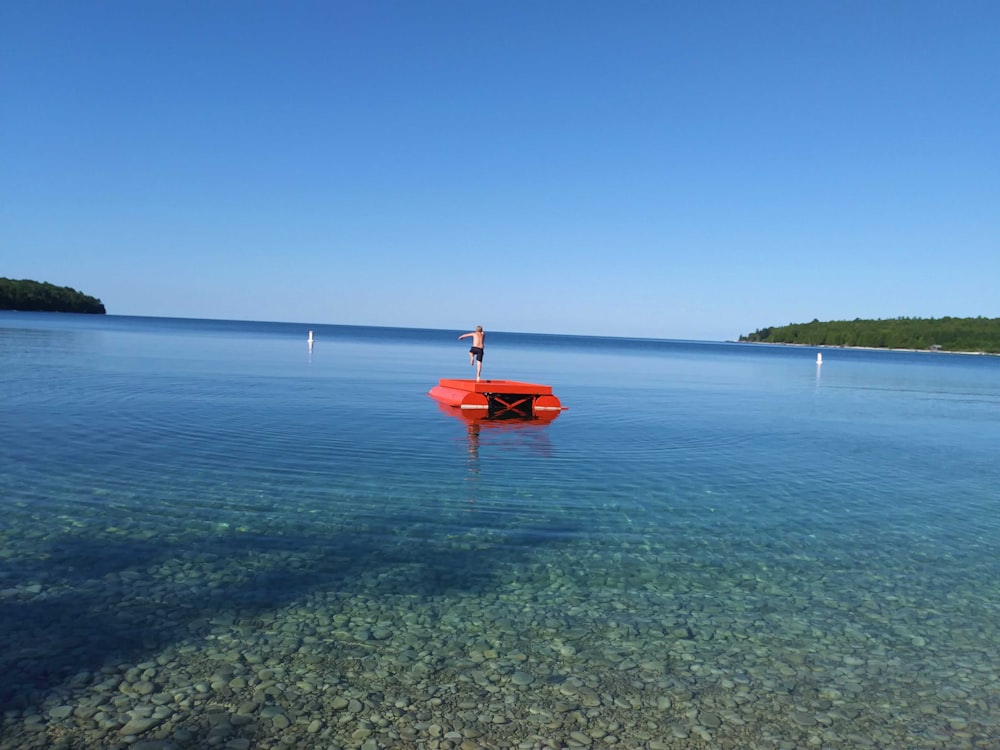 person in red shirt standing on orange kayak on sea during daytime