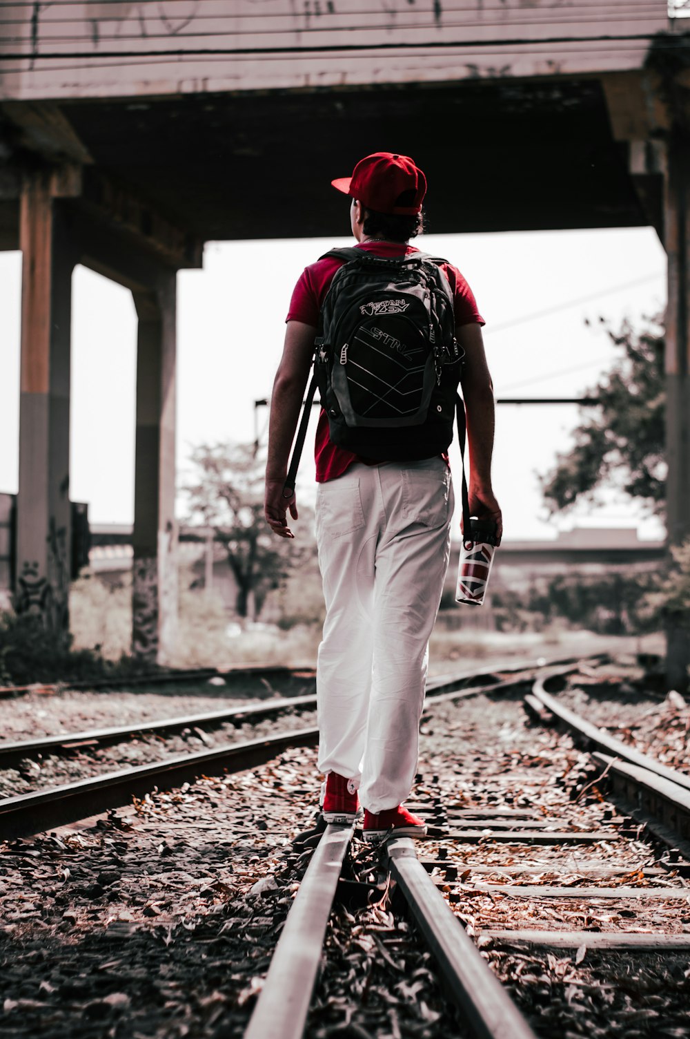 hombre con mochila roja y negra caminando sobre el riel del tren durante el día