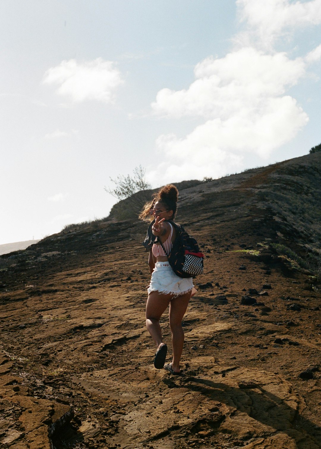 woman in black and white stripe shirt and white shorts standing on brown rock during daytime