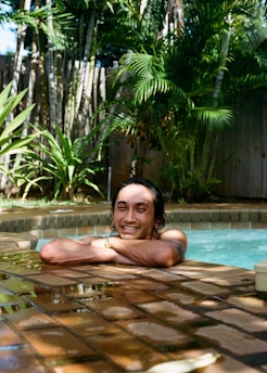Portrait of a smiling man standing by a tropical pool with lush greenery in the background.