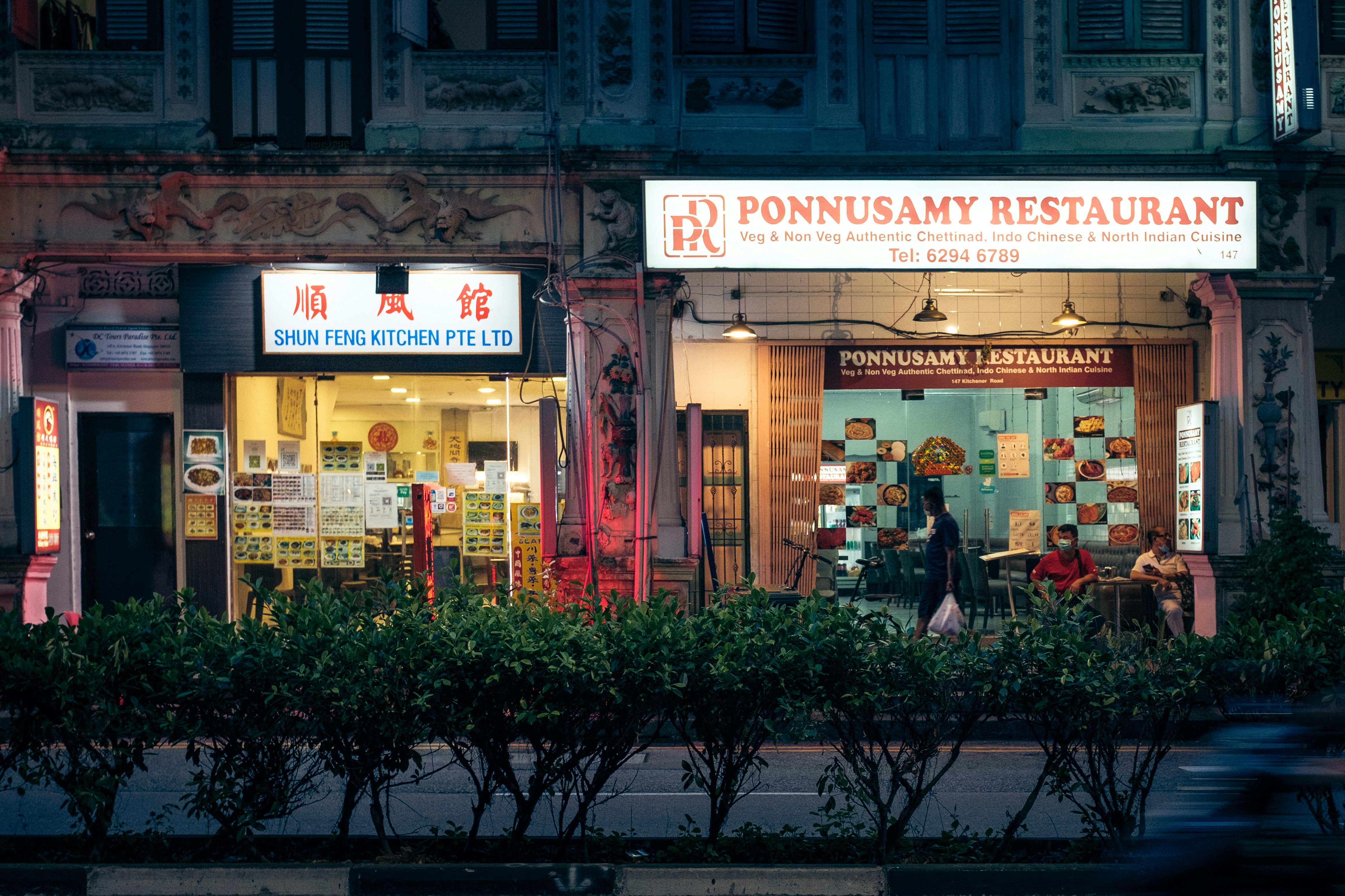 man in black jacket sitting on black bench in front of store during daytime, Exterior of the Chinese restaurant next to the Indian restaurant