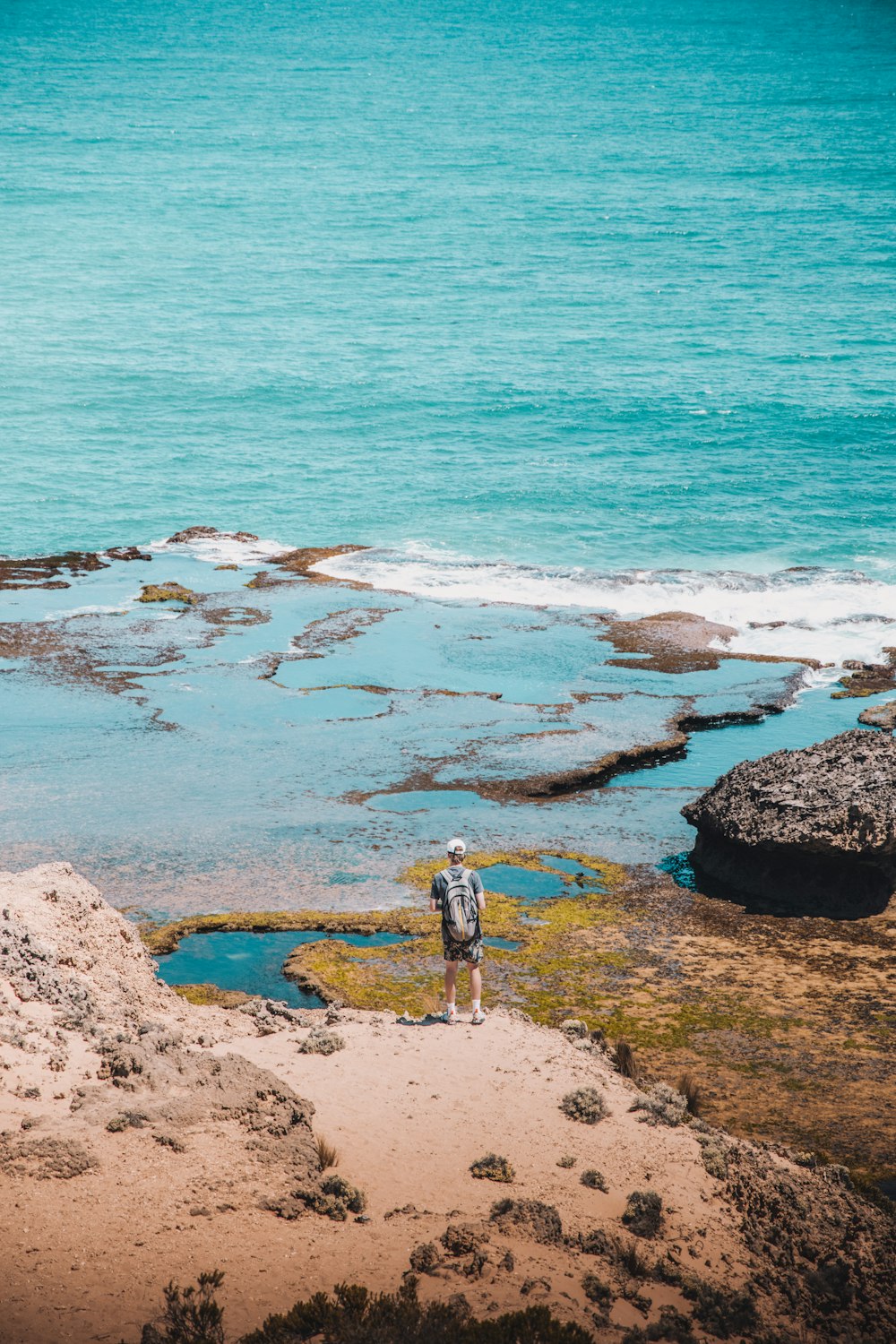 person in white shirt standing on brown rock near body of water during daytime