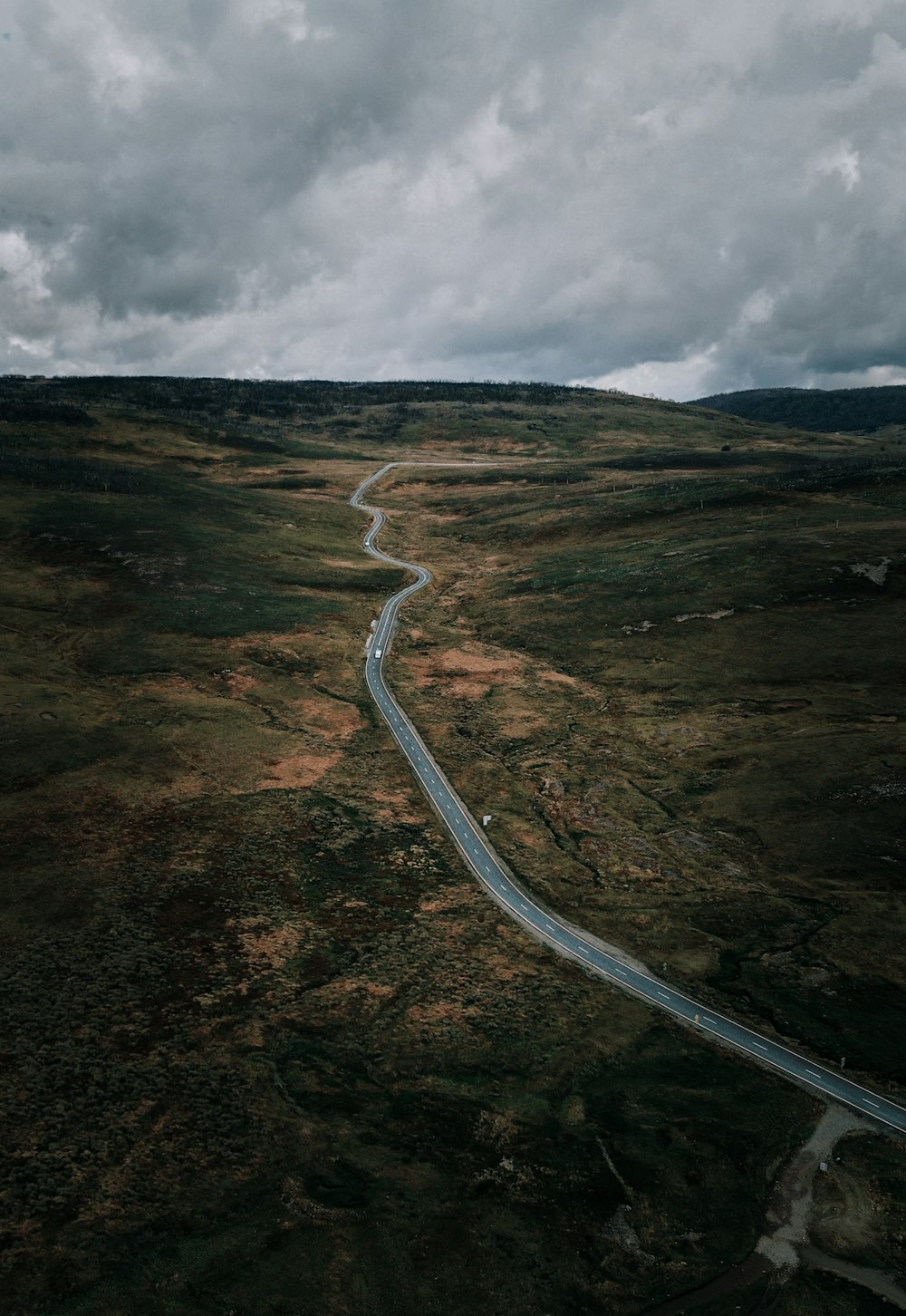 gray asphalt road on brown and green mountain under gray cloudy sky during daytime