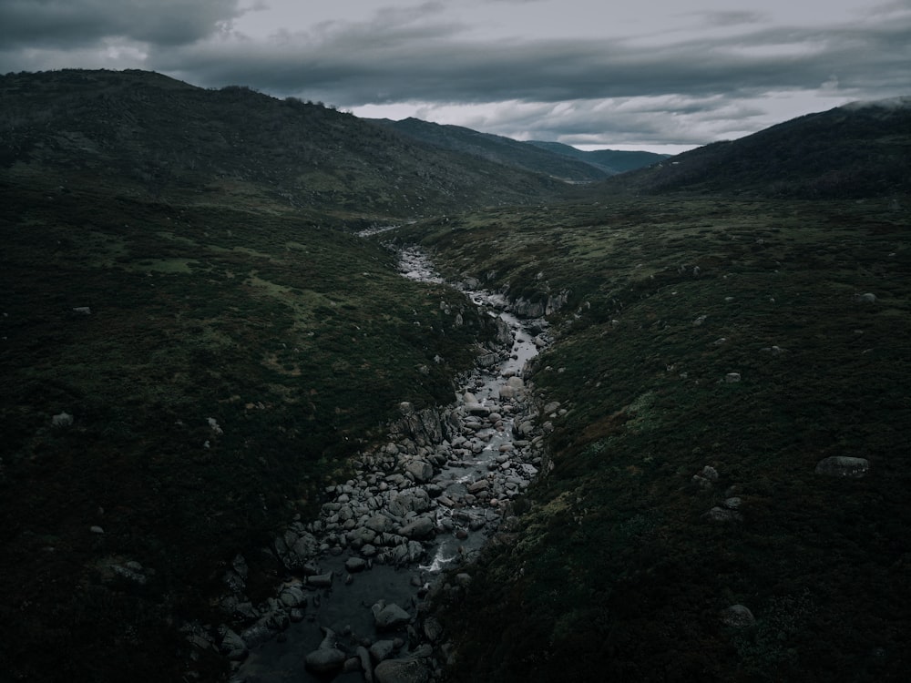 river between green mountains under white clouds during daytime