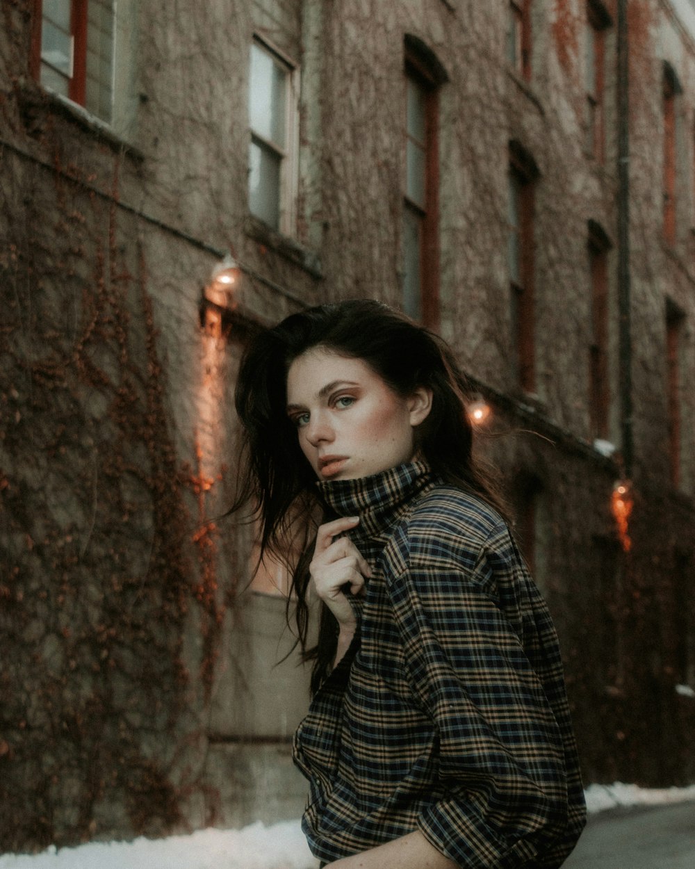 woman in black and white plaid dress shirt standing beside brown wall