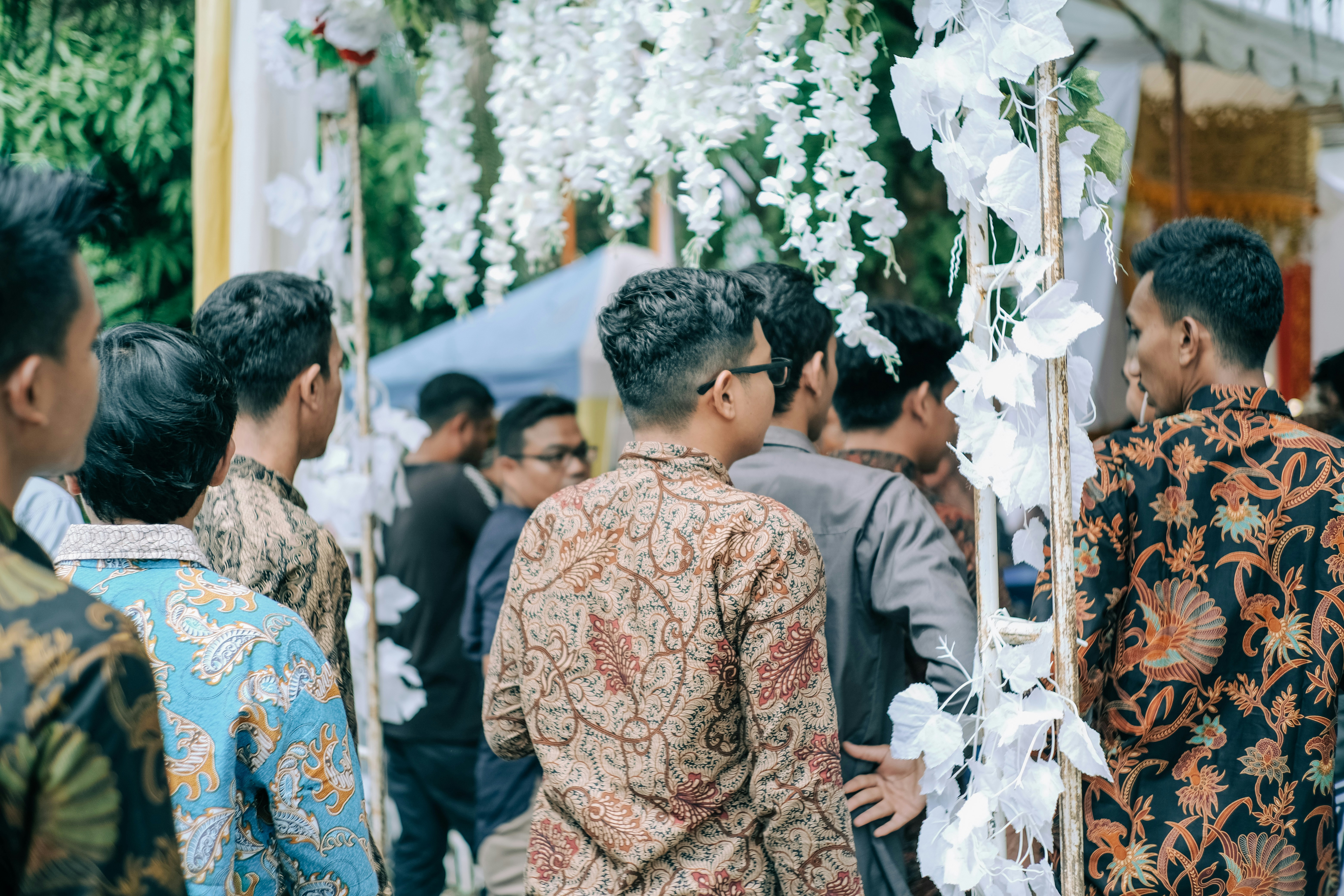 Pria dengan kemeja bunga coklat dan biru berdiri di dekat orang-orang di siang hari