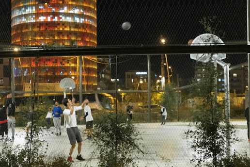 A lively grassroots basketball game with young players in action under bright city lights.