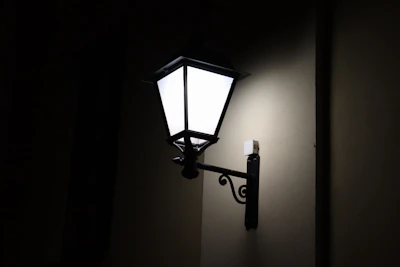 A vintage-style wall lantern casting a warm amber light on a rustic wooden fence