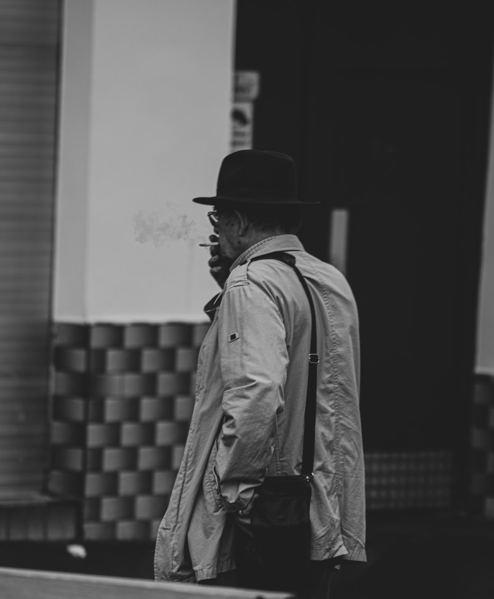 grayscale photo of woman in coat and hat walking on sidewalk