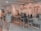A cozy café interior with a rustic and bohemian decor style, featuring rattan chairs and pendant lights, a counter with a barista, and patrons sitting on high stools. The walls are adorned with artworks and potted plants, creating a warm and inviting atmosphere.