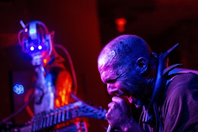 A vibrant stage setup with anime posters behind the bald singer performing live.