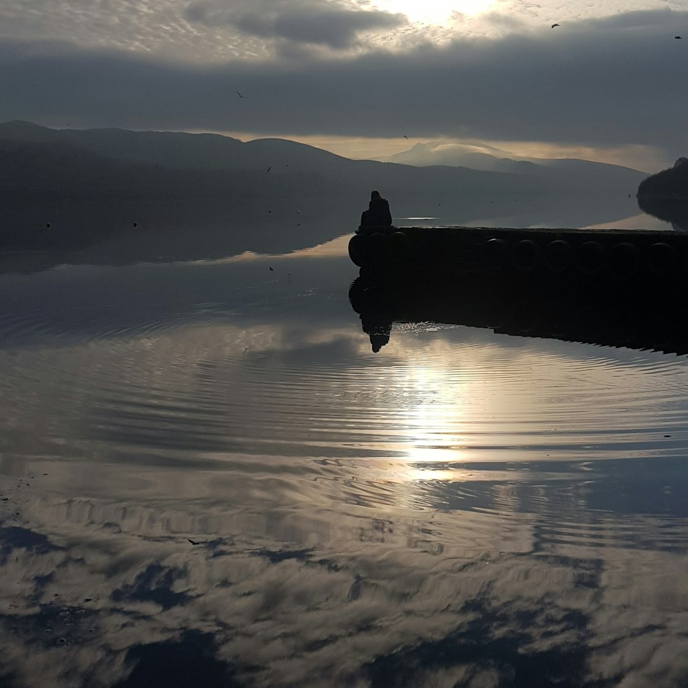 silhouette d’homme debout sur le bateau sur l’eau pendant la journée