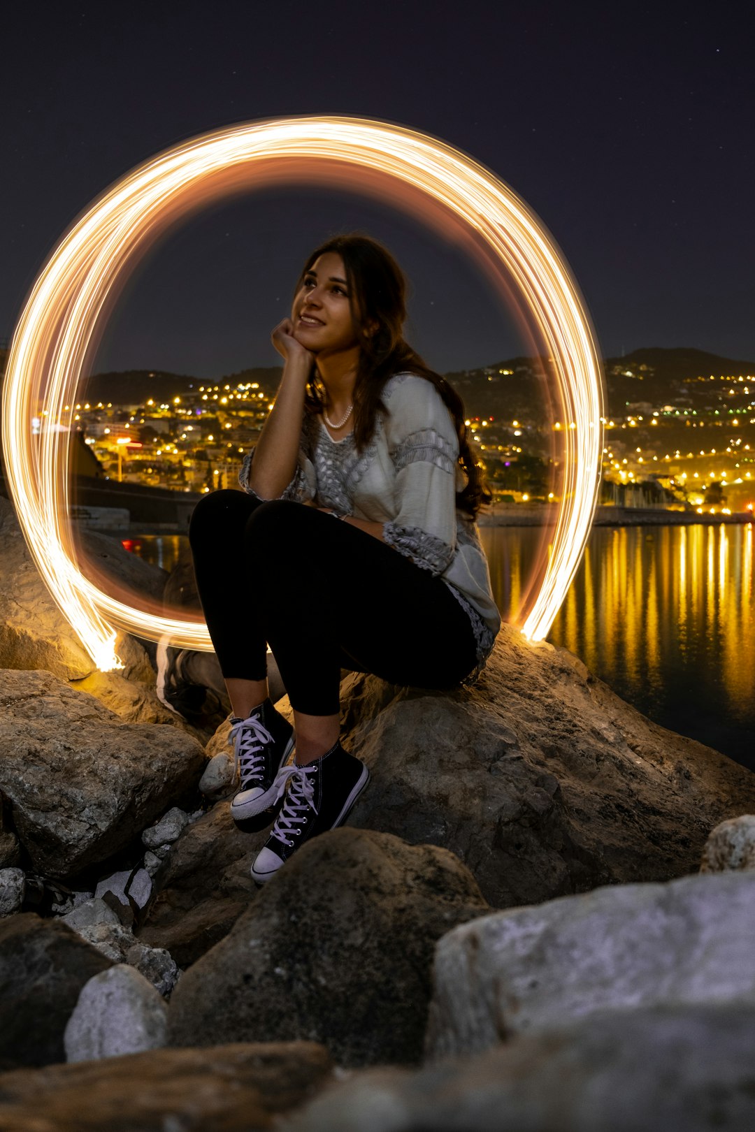 woman in white long sleeve shirt sitting on rock near body of water during night time