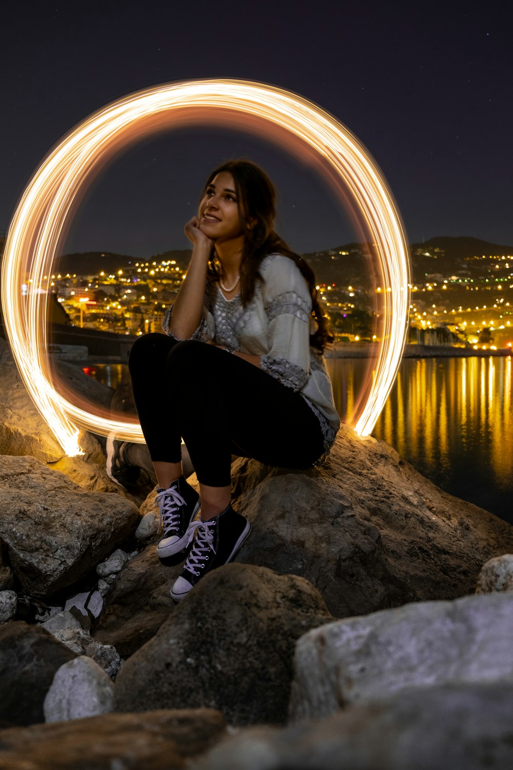 woman in white long sleeve shirt sitting on rock near body of water during night time