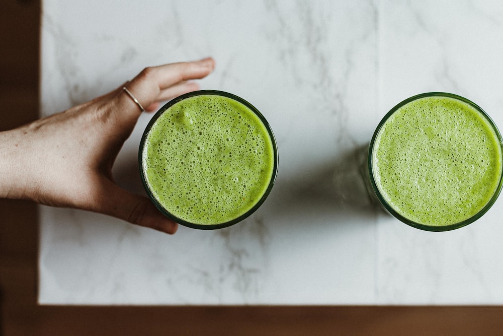 person holding green liquid in clear drinking glass