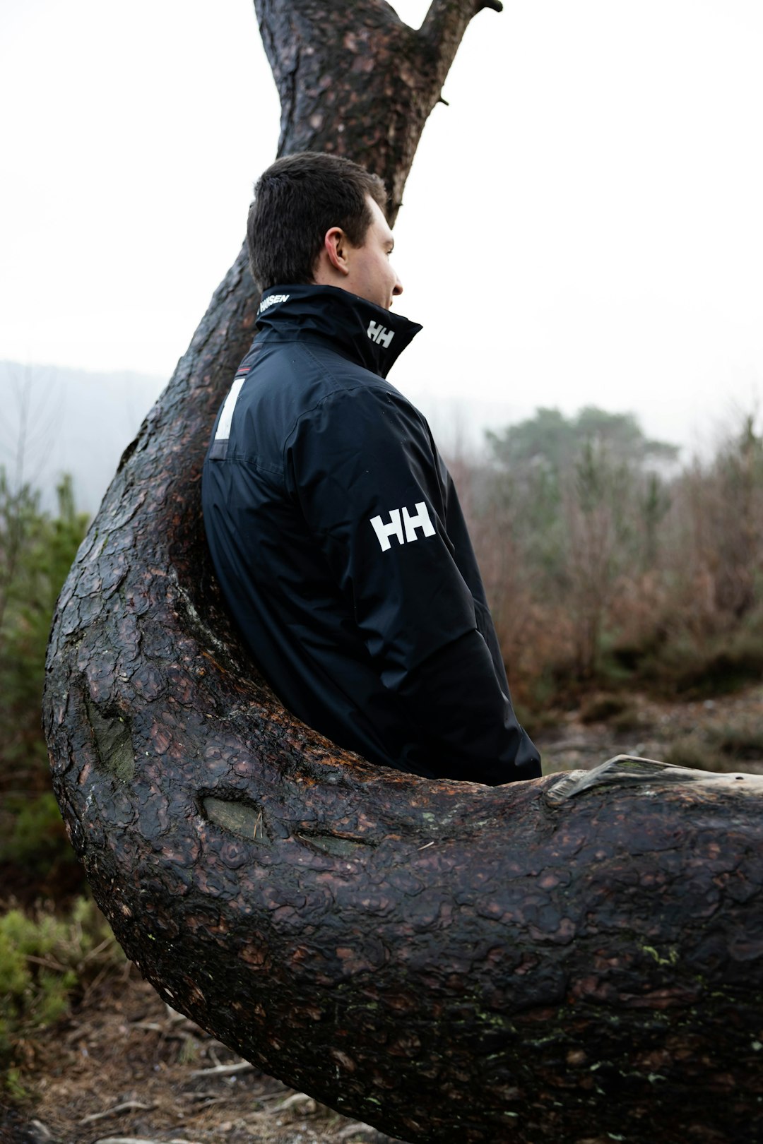 man in black jacket sitting on brown tree trunk during daytime