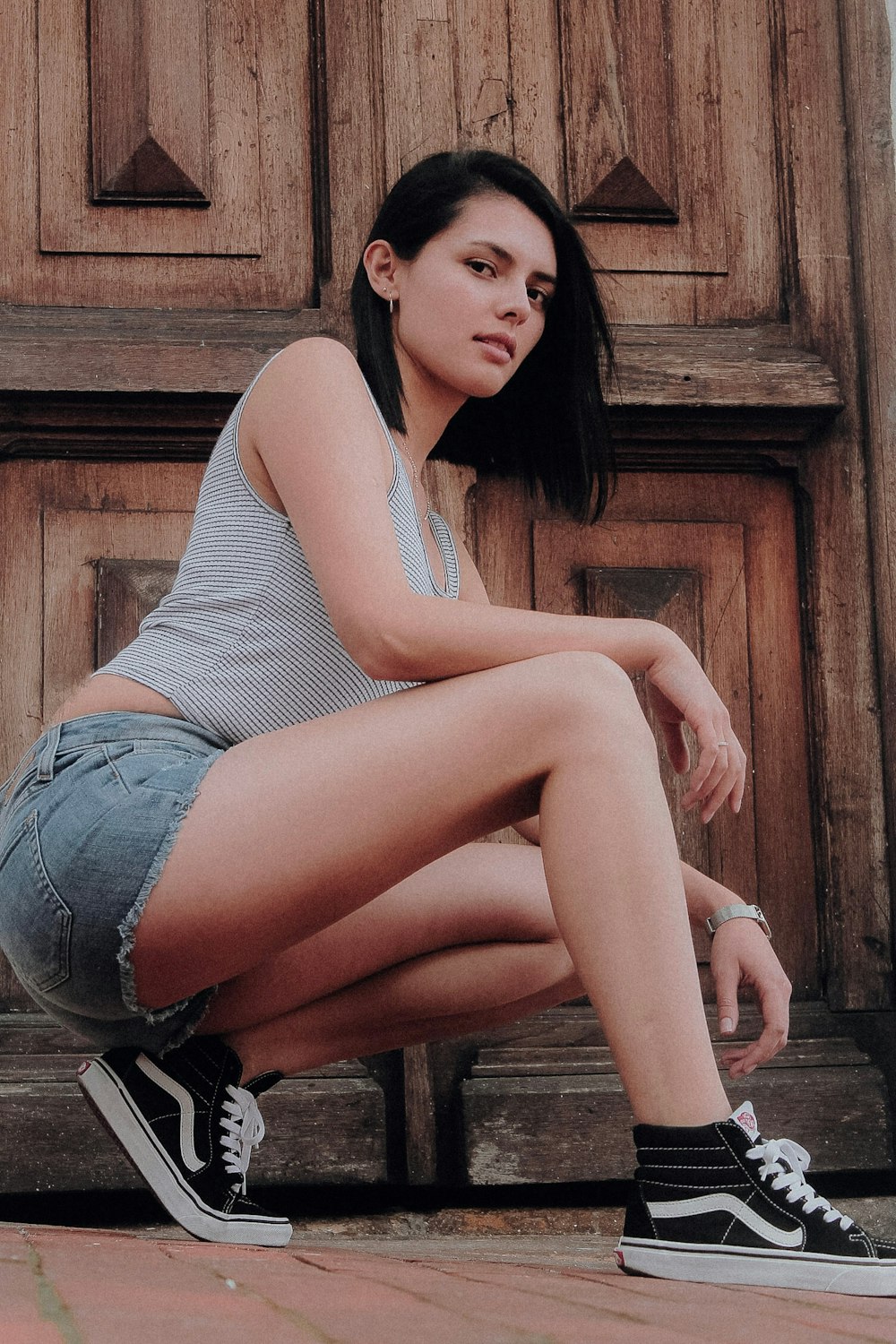 woman in gray tank top and blue denim shorts sitting on brown wooden bench
